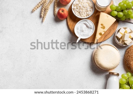 Religious Jewish holiday Shavuot concept with dairy products, cheese, bread, milk, wheat crops and fruits on white background, copy space, top view. Happy Shavuot. Royalty-Free Stock Photo #2453868271