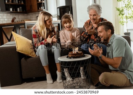 Heartwarming scene unfolds as a multi-generational family gathers on a couch to present a birthday cake to a delighted grandmother, creating memories to cherish Royalty-Free Stock Photo #2453870969