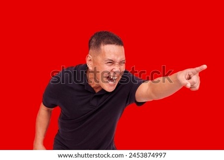 An enraged Asian man aggressively pointing and yelling, with strong heated emotion. Red background. Royalty-Free Stock Photo #2453874997
