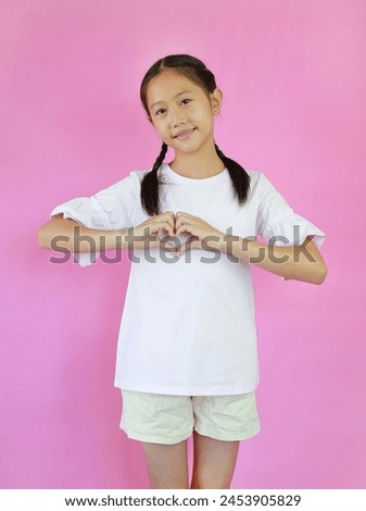 Portrait of Asian young girl child making heart figure love sign with fingers isolated on pink studio background.