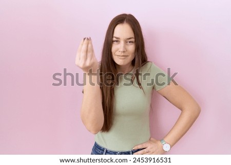 Beautiful brunette woman standing over pink background doing italian gesture with hand and fingers confident expression 