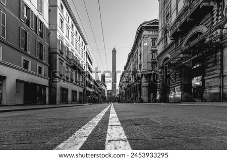 Monochrome image of a Bologna street taken from a low angle, focusing on the converging road lines that lead toward the towering Asinelli Towers in the background Royalty-Free Stock Photo #2453933295