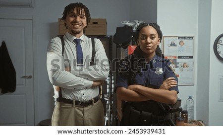 A man and a woman, a detective and a policewoman, standing with crossed arms in a police station office, facing the camera. Royalty-Free Stock Photo #2453939431