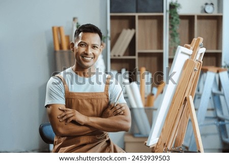 Creative painter painting in an art studio. Artistic young man working on a new painting. Cheerful young artist looking at the camera.