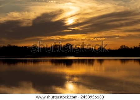 The sky and the lake are red-tinged during sunset, a beautiful sunset on the lake in early spring Royalty-Free Stock Photo #2453956133