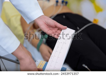 A caregiver is attentively checking a patients vitals with an EKG readout in their hand. Royalty-Free Stock Photo #2453971357