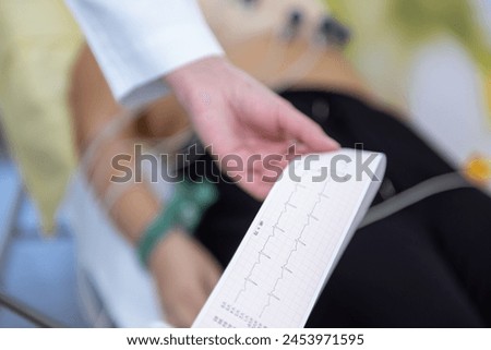 A caregiver is attentively checking a patients vitals with an EKG readout in their hand. Royalty-Free Stock Photo #2453971595