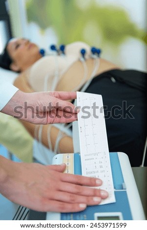 A caregiver is attentively checking a patients vitals with an EKG readout in their hand. Royalty-Free Stock Photo #2453971599