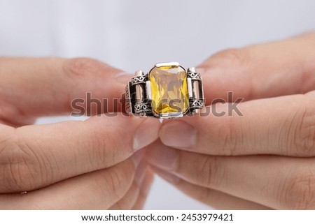 Ring with colorful stones in the hand of a well-groomed man in a white shirt. Photo of men's jewelry for e-commerce, social media, sale.