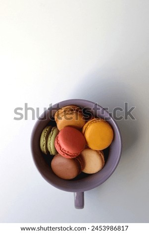 Purple cup filled with pastel macarons on white background. Top view.