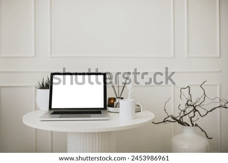 Laptop and white mug with tea on a table. Workspace in a modern room with white walls.