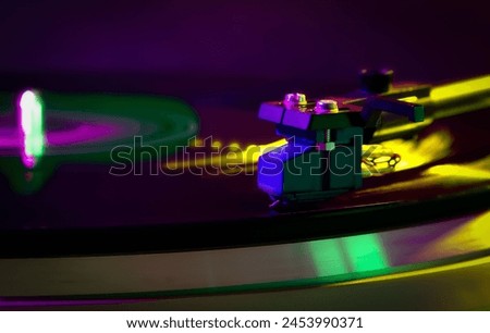 
A multi-coloured image featuring a close-up of a gramophone pick-up, with the turntable blurred from its rotation. Colours include yellow, green, purple, and blue, creating a vibrant visual compo. Royalty-Free Stock Photo #2453990371
