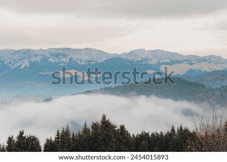 The vast mountain range is shrouded in a thick layer of clouds, creating a mystical and ethereal atmosphere. The peaks jut out like towering giants through the billowy white blanket Royalty-Free Stock Photo #2454015893