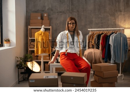 Confident female entrepreneur in eyeglasses and trendy attire stands proudly in her clothing store