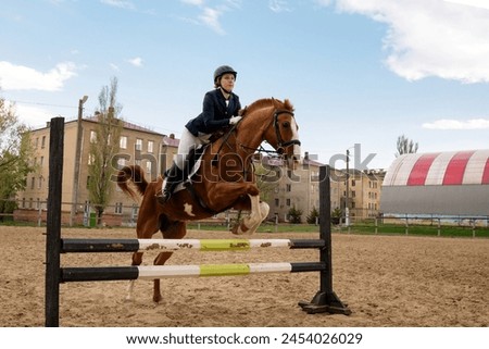 Rider jumping horse over obstacle, equestrian sport. Riding session. Female jockey in uniform riding equine. Show jumping. Horseback riding school Royalty-Free Stock Photo #2454026029
