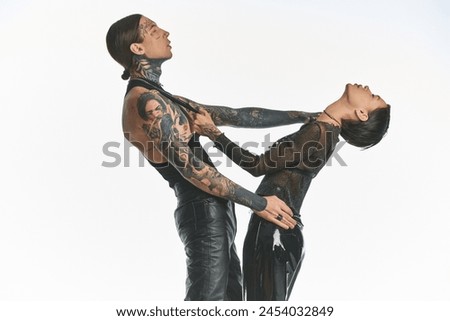 A young, stylish, and tattooed couple standing next to each other in a studio against a grey background.