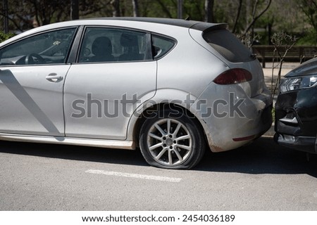 Detail of the concept of the flat tire of a gray car parked on the street that is old and dirty, unattended. Maybe abandoned or stolen but it is a problem in the city Royalty-Free Stock Photo #2454036189