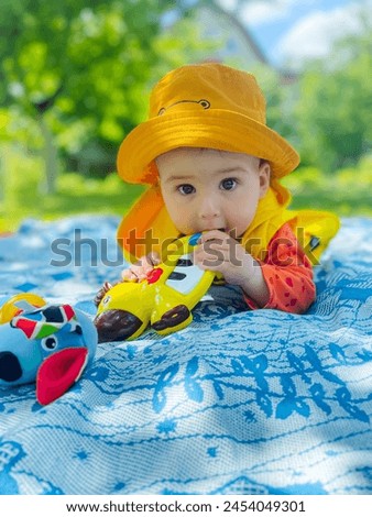 A baby wearing a yellow hat and a yellow jacket laying on a blanket. The baby has a serious expression on its face
