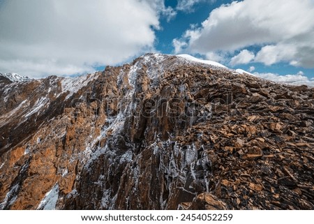 Scenic view to big rocky mountain top in freshly fallen snow close up. Closeup of large snowy stony peak in sunlight under cloudy sky. Atmospheric scenery of snow-covered sharp rocks in high mountains Royalty-Free Stock Photo #2454052259