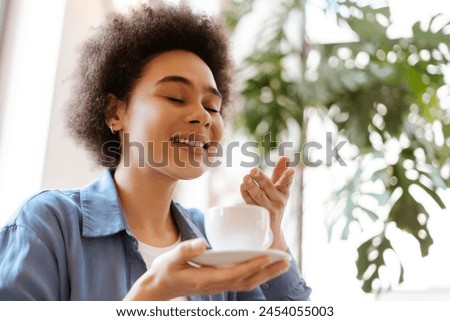 Happy smiling African American woman with curly hair holding cup of coffee, sniffing fragrant aroma closeup of copy space. Breakfast concept, advertisement Royalty-Free Stock Photo #2454055003