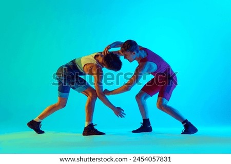 Athletes in motion, competitive young men, wrestlers in motion, competing, training against blue background in neon light. Concept of combat sport, martial arts, competition, tournament, athleticism