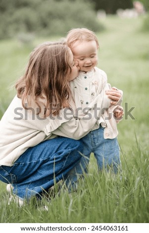 Child girl kissing baby wearing stylish clothes over green grass lawn outdoor. Summer season. Childhood. 