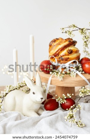 Festive table setting with ceramic bunny, red eggs, candles and Easter pastries, vertical photo. Easter holiday concept