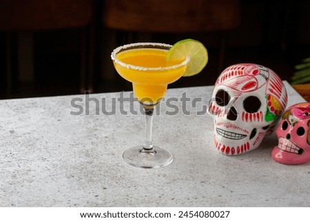 An array of margarita cocktails in different flavors, garnished with lime, beside vibrant sugar skulls, symbolizing the Mexican Day of the Dead