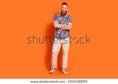 Full size photo of pleasant cool man wear stylish shirt white pants holding arms crossed smiling isolated on orange color background