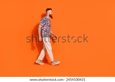 Full size photo of confident nice man with red beard wear stylish shirt walk empty space look at sale isolated on orange color background