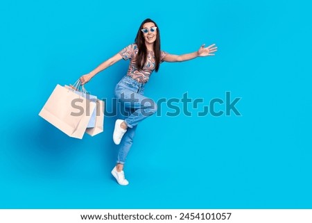 Full size photo of pretty young girl running hold shopping bags empty space wear trendy colorful clothes isolated on blue color background