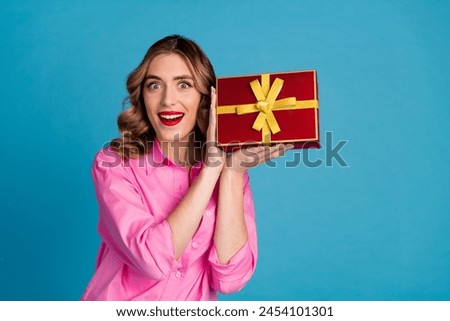 Photo portrait of pretty young girl hold excited giftbox wear trendy pink outfit hairdo isolated on blue color background