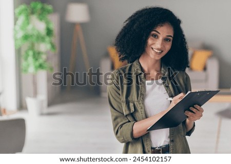 Photo of pretty young woman hold clipboard write pen wear khaki shirt modern interior house indoors