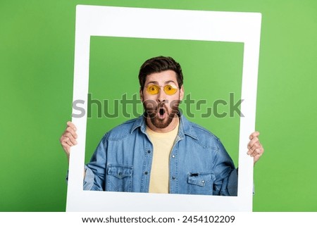 Photo of positive impressed guy dressed jeans shirt holding photo frame isolated green color background