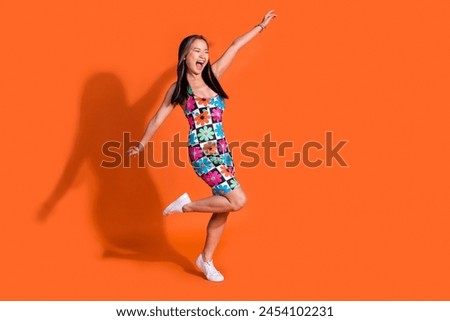 Full size photo of positive cheerful woman wear print stylish dress look at promotion empty space isolated on orange color background