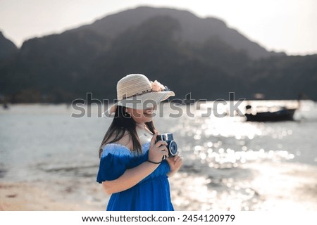 Woman enjoying the beach in summer, wearing a hat, smiling, with a  holding a camera taking pictures of the seascape
