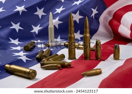 Closeup of cartridges and bullets of different sizes arranged on top of American flag with stars and stripes