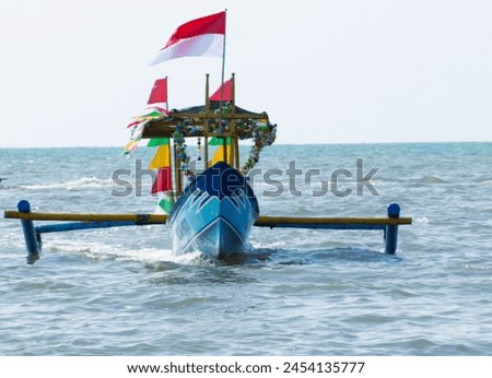 Pemalang, Central Java, Indonesia - April 15th 2024. Tourist boat with big indonesian flag sailing on Widuri beach, Pemalang, Central Java, Indonesia. Royalty-Free Stock Photo #2454135777