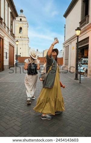 Two tourists walk down a street and one of them takes pictures with her phone in Lima Peru.