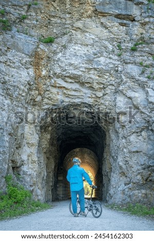 Male cyclist with a folding bike on Katy Trail at a tunnel near Rocheport, Missouri, spring scenery. The Katy Trail is 237 mile bike trail converted from an old railroad. Royalty-Free Stock Photo #2454162303