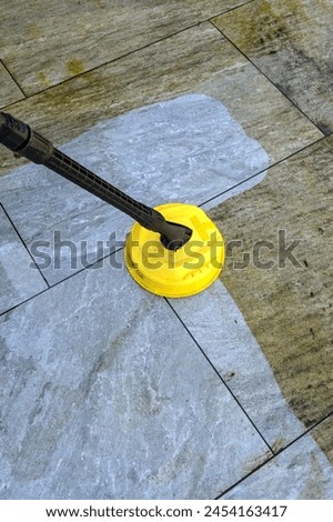 Pressure jet washer being used to clean porcelain tiles on a garden patio showing the difference before and after cleaning