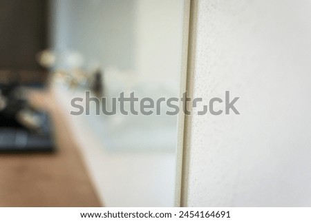 Detail of tempered white glass used as a backsplash in a new modern kitchen with oak countertop, shallow depth of field 