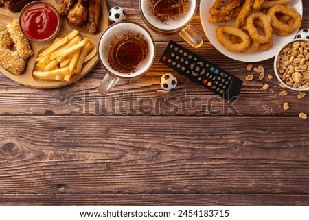 An inviting display of game day snacks including fries, chicken wings, onion rings, and beer, arranged neatly next to a remote control and mini soccer balls