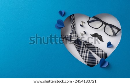 Creative Father's Day flat lay with a stylish tie, glasses, and mustache set against a heart-shaped cutout and blue background, symbolizing love and appreciation