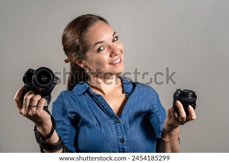 Young woman comparing a professional camera with a new lens.  Young woman deciding between buying a new camera or a new lens. Woman with a camera and lens in her hands. 
