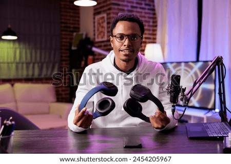 Portrait of technology reviewer recording headphones comparison episode using professional microphone in living room studio. Experienced content creator filming audiophiles channel vlog Royalty-Free Stock Photo #2454205967