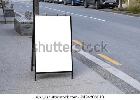 A blank white outdoor advertising stand or sandwich board mockup template. Background texture of a clear street signage board placed outdoors on a pedestrian sidewalk. Urban city environment.