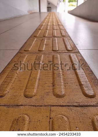 Brownish yellow tactile paving with an embossed texture, installed on the floor of the building to facilitate and guide people with disabilities