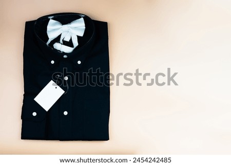 Black folded mens shirt with blank tag label mockup and white bow tie. Fashion branding mockup scene