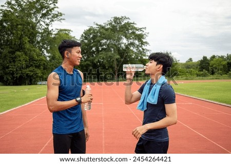 Two young Asian teenage athletes drinking water and resting during a break in track and field training, highlighting the importance of hydration Royalty-Free Stock Photo #2454264421